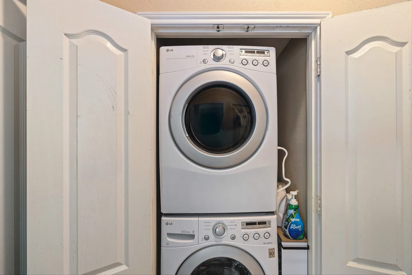 A stacked white LG washer and dryer unit inside a closet behind open white paneled doors.