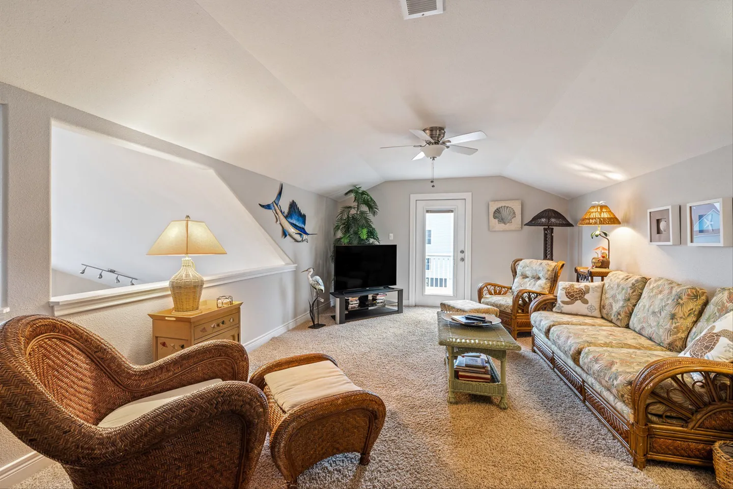 Upstairs loft living area featuring wicker seating, patterned floral cushions, carpeted flooring, and a TV.
