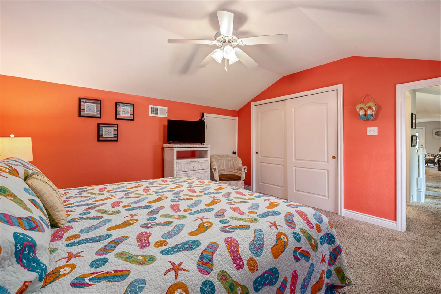 Bedroom with bright coral walls, carpeted floor, ceiling fan, and a bed with a flip-flop pattern quilt.