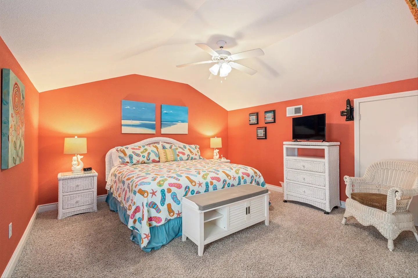 Bedroom with bright orange walls, vaulted ceiling, and white wicker-style furniture including a bed, nightstands, and a dresser with a television.