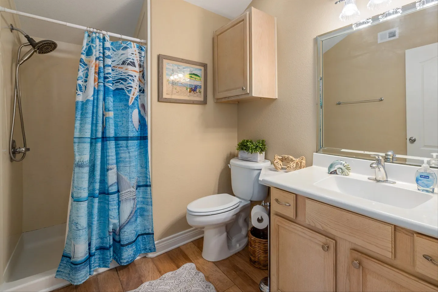 Bathroom with a walk-in shower featuring a coastal themed curtain, a toilet, an upper cabinet, and a vanity with a large mirror.