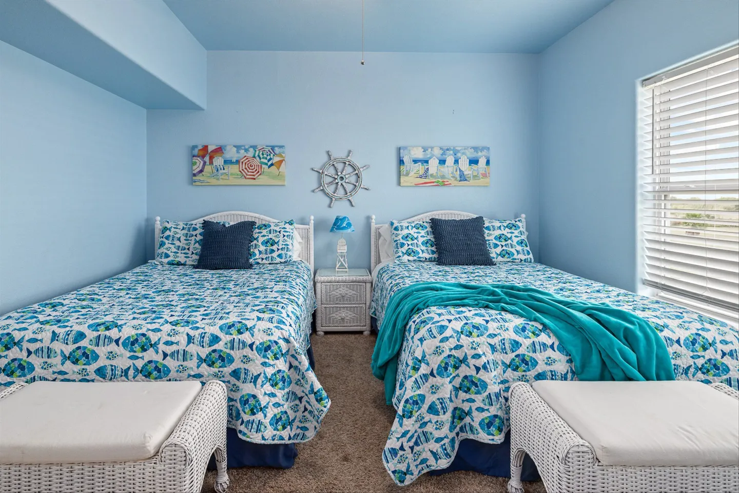 Bedroom with blue walls, carpeted floor, two matching beds covered in fish-patterned quilts, and white wicker accents.