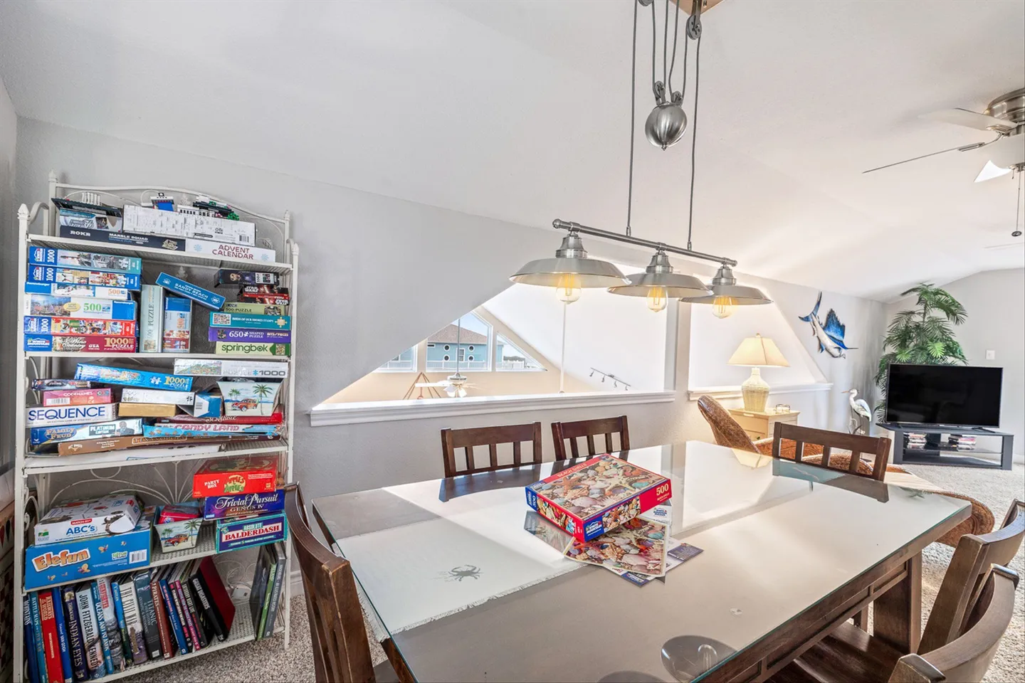 Game and dining area with a glass-topped table, three-light pendant, and shelves full of board games and puzzles.