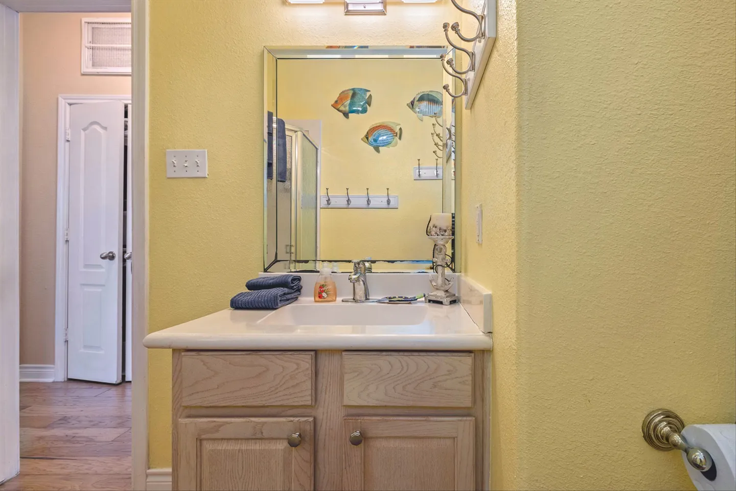 Bathroom vanity with a light wood cabinet, white countertop, and beveled mirror on a yellow wall.
