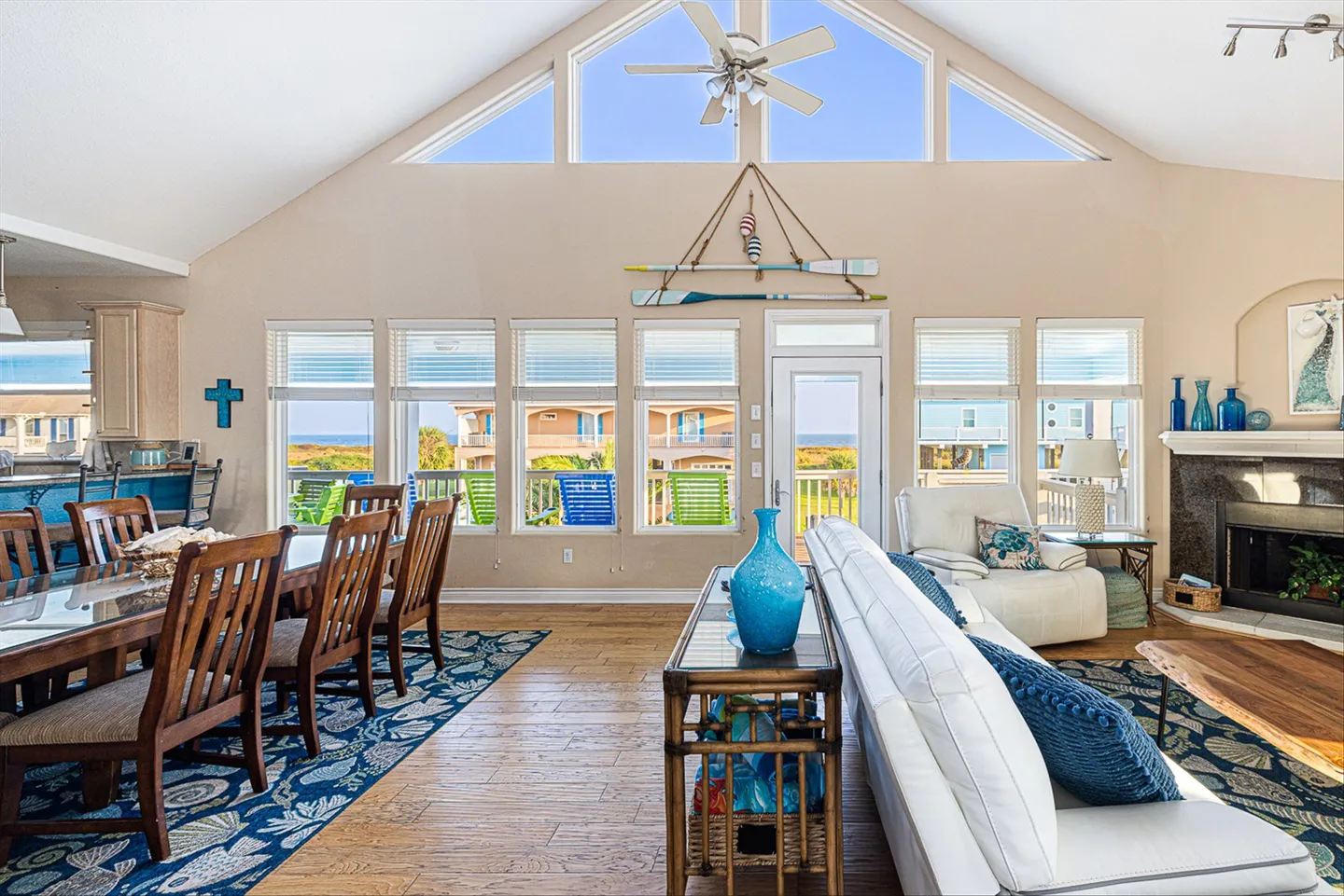 Open living and dining area with vaulted ceiling, large windows showing an outdoor deck, and a white sofa.