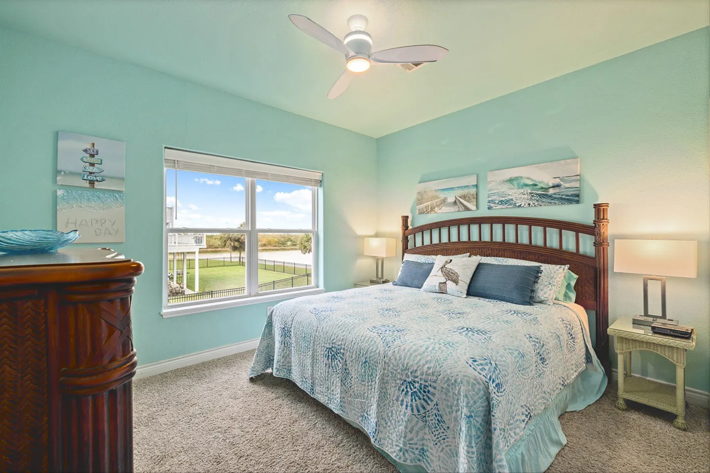 Bedroom with aqua walls, carpeted floor, ceiling fan, and a large bed with a wooden headboard next to a window showing outdoor views.