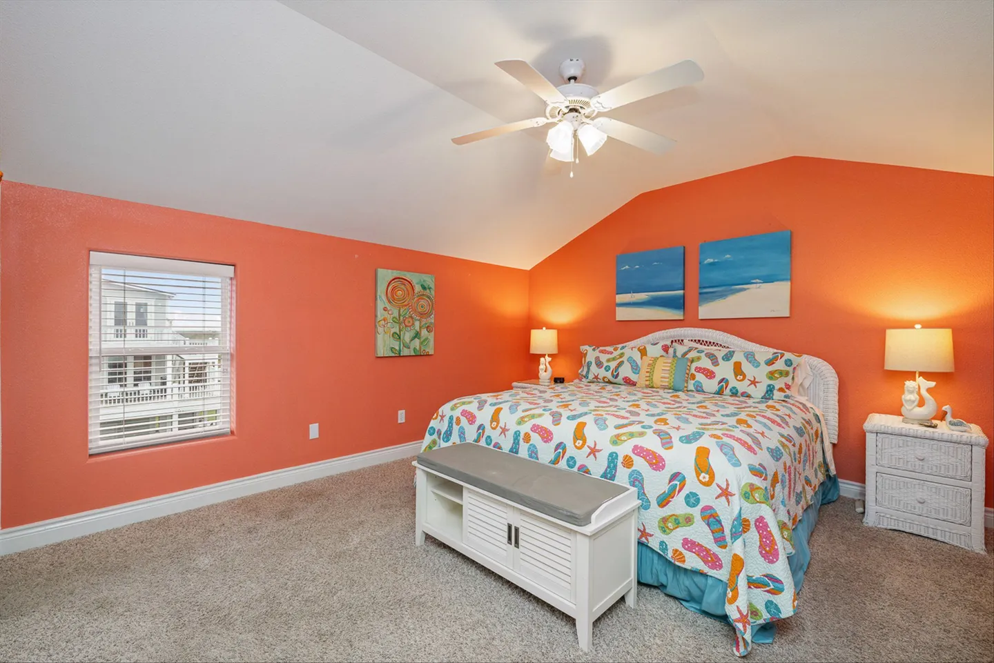 Bedroom with bright coral walls, carpet, a bed with a flip-flop pattern quilt, a white bench, and a ceiling fan.