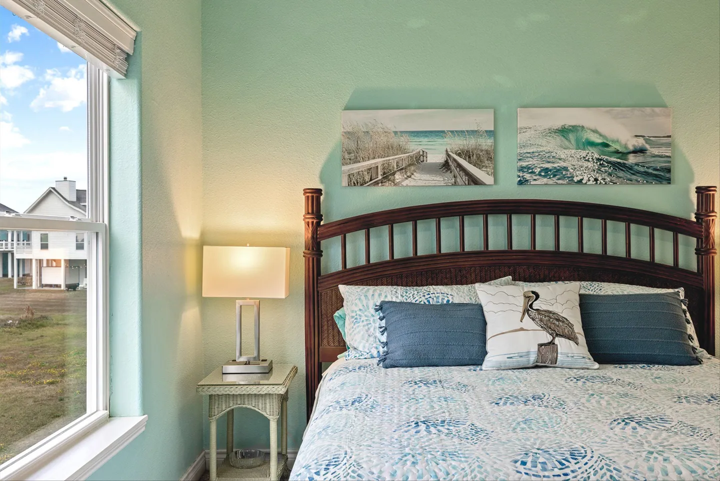 Bedroom with light green walls, a dark wood headboard, coastal-themed bedding, and a window looking outside.
