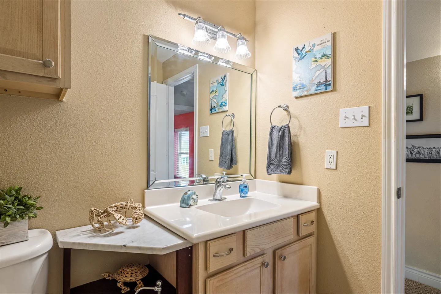 Bathroom vanity with a light wood cabinet, white sink, beveled mirror, and coastal decorations.