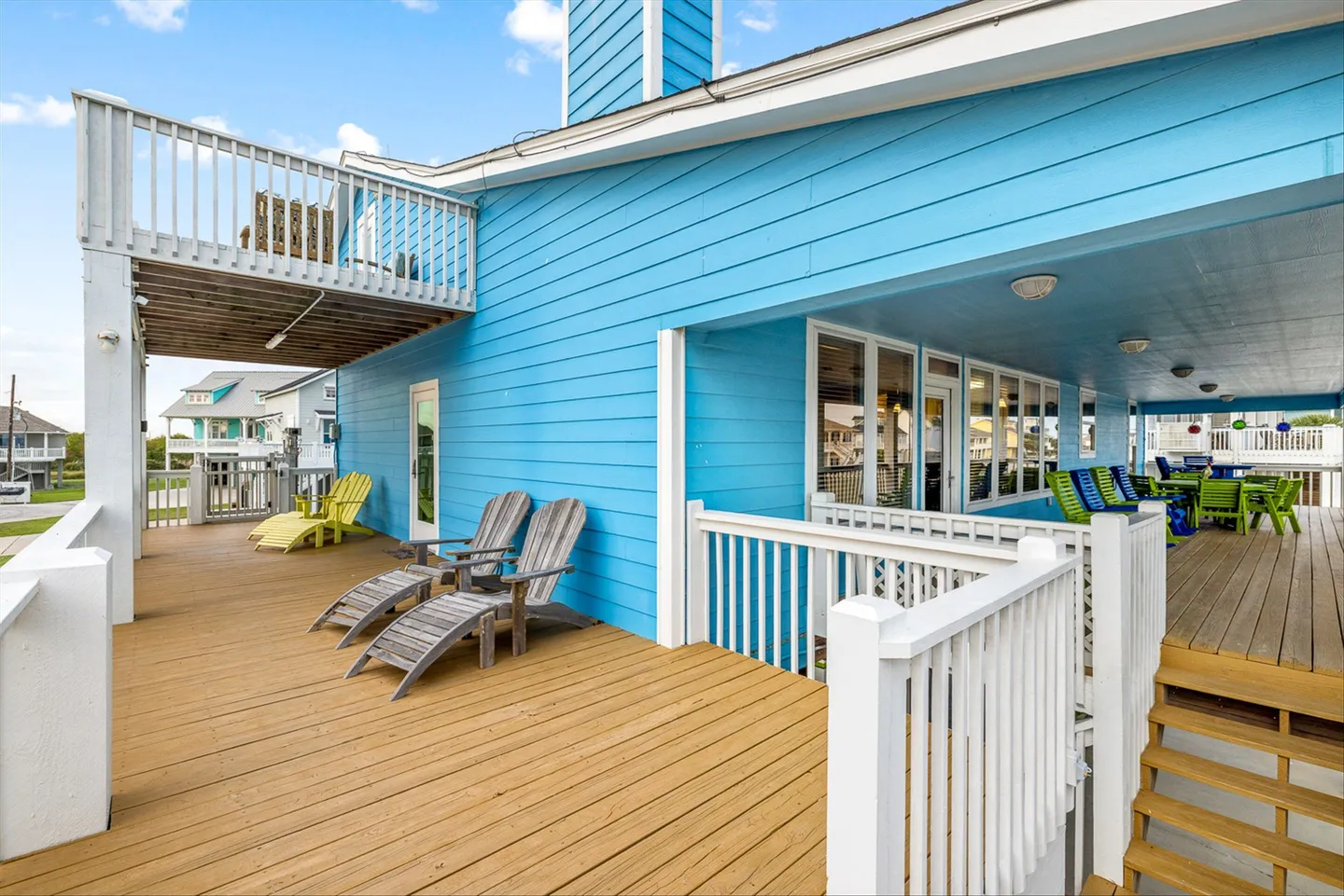 Exterior wooden deck with lounge chairs against a bright blue-sided coastal home under a clear sky.