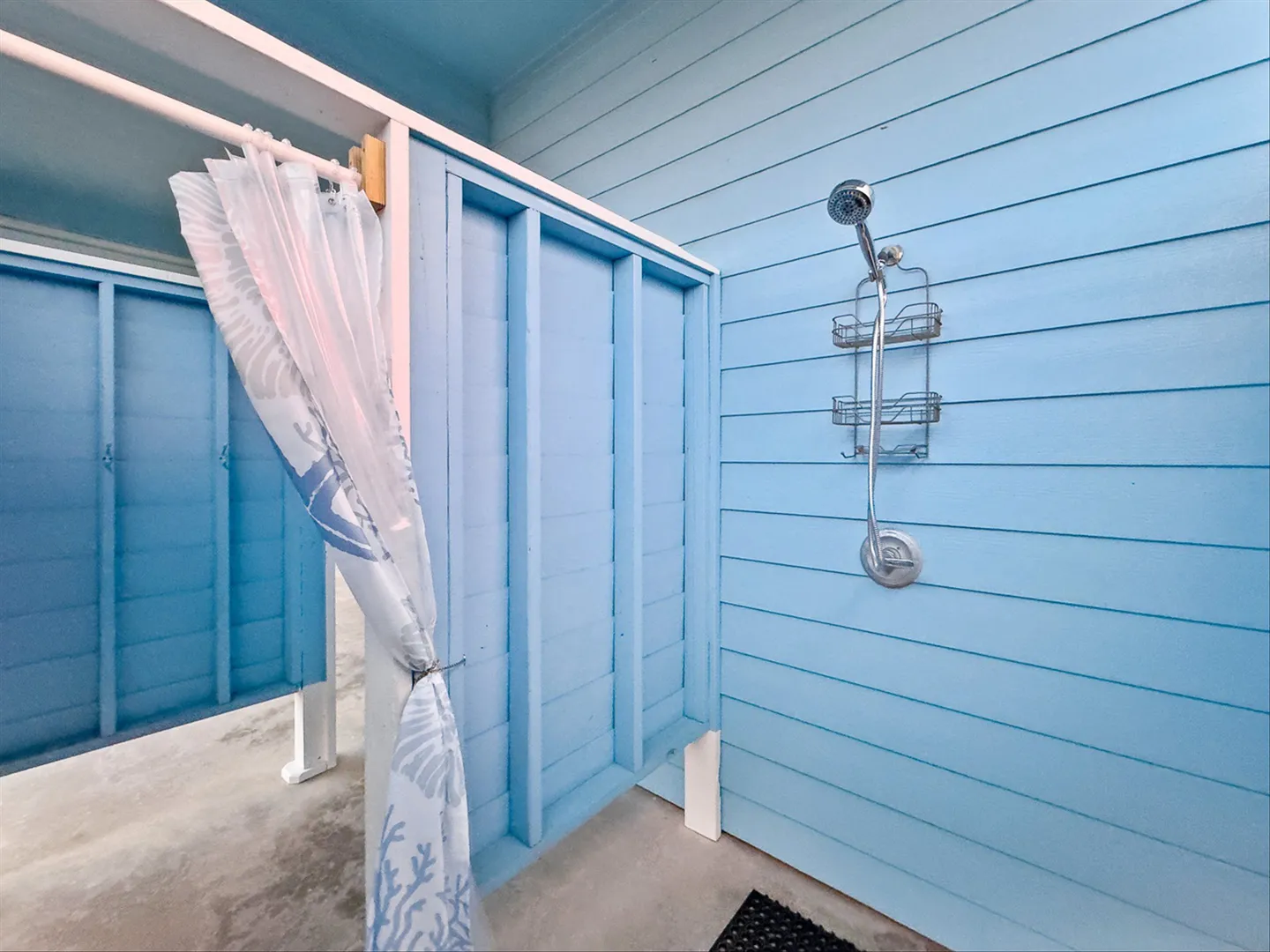 Outdoor shower stall with light blue siding, a wall-mounted showerhead, and a white curtain.