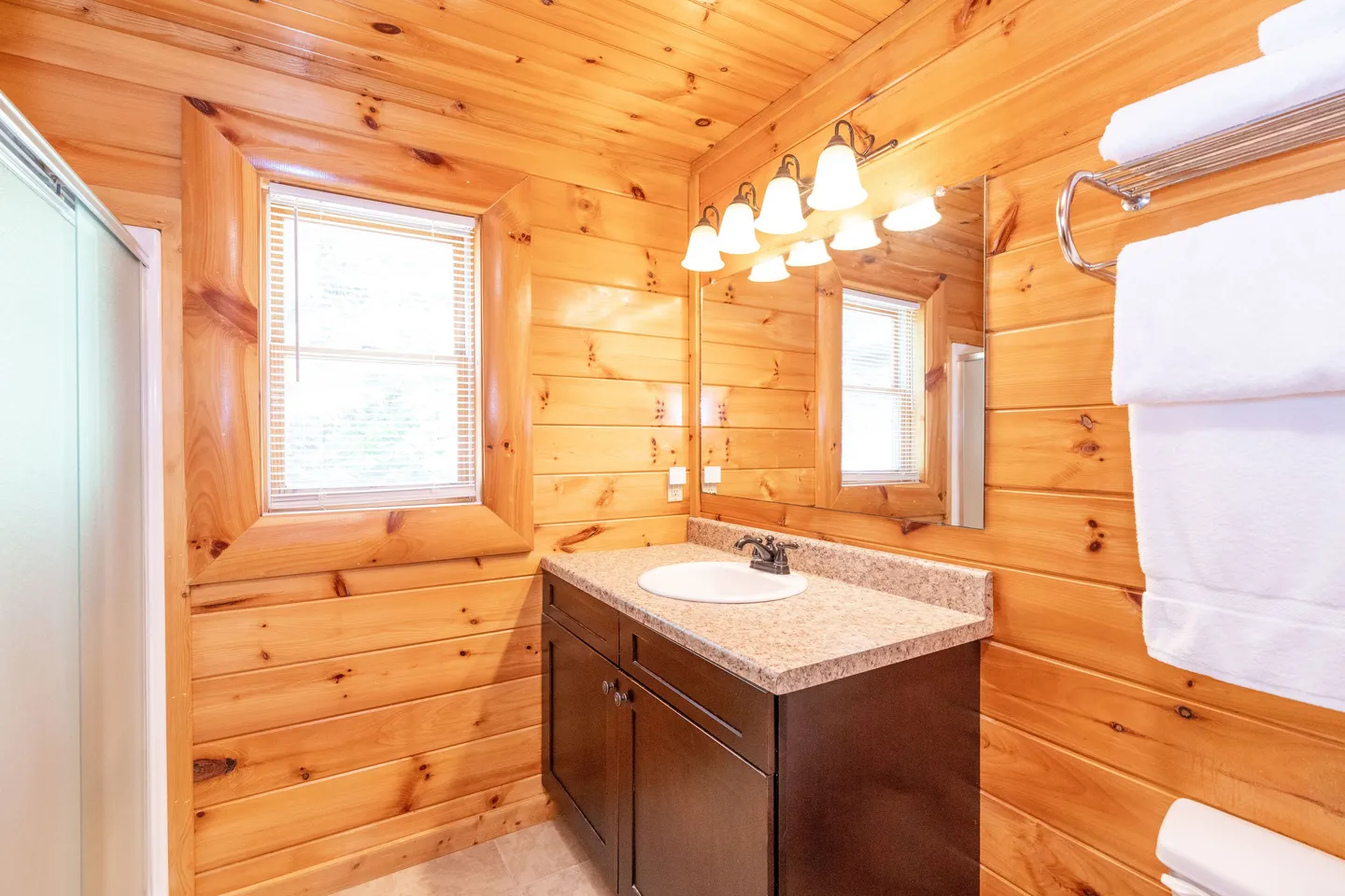 Bathroom with wood-paneled walls, a dark vanity with a speckled countertop, a mirror, and an overhead light fixture.