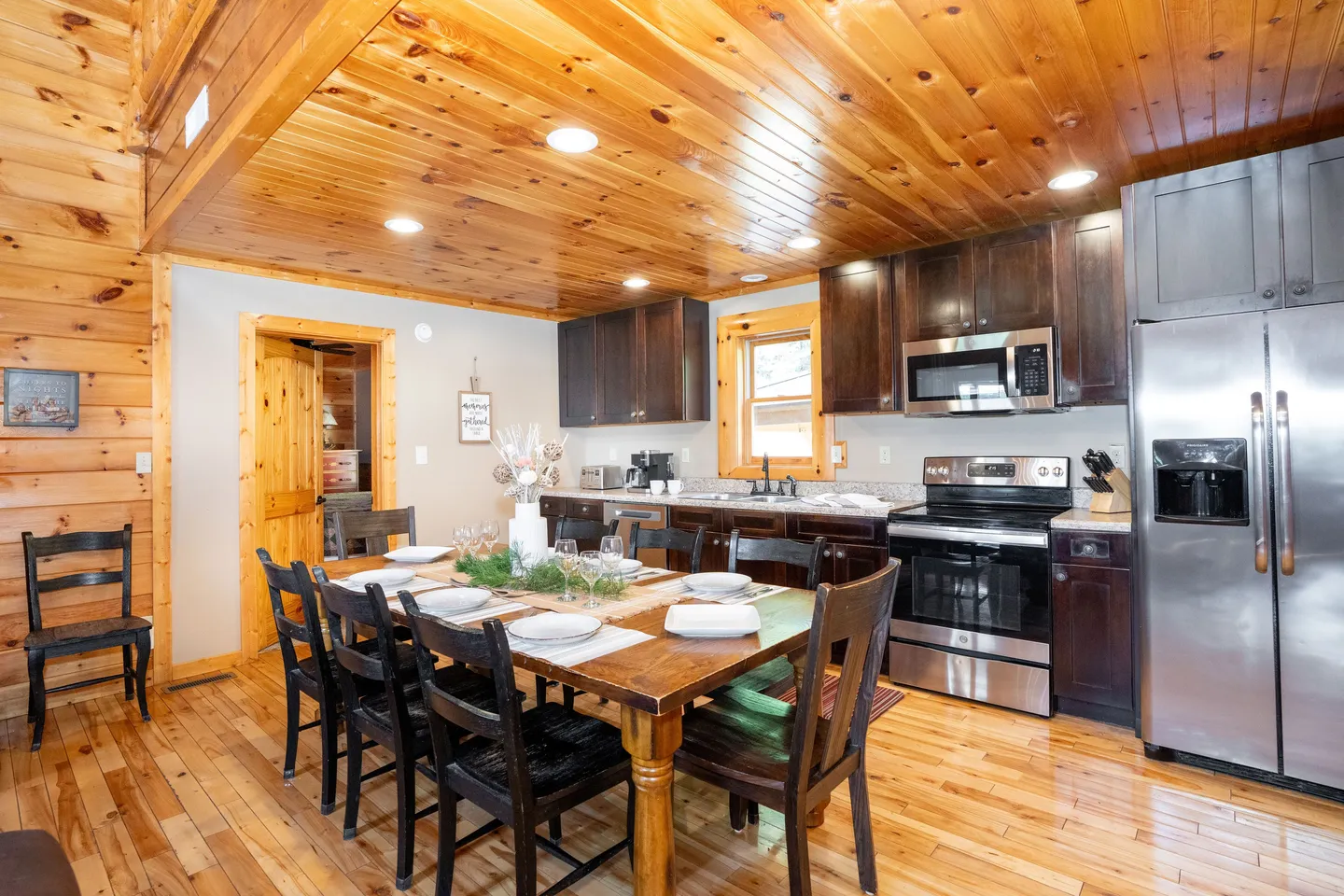 Dining area with a wooden table and chairs adjacent to a kitchen with dark cabinetry and stainless steel appliances.