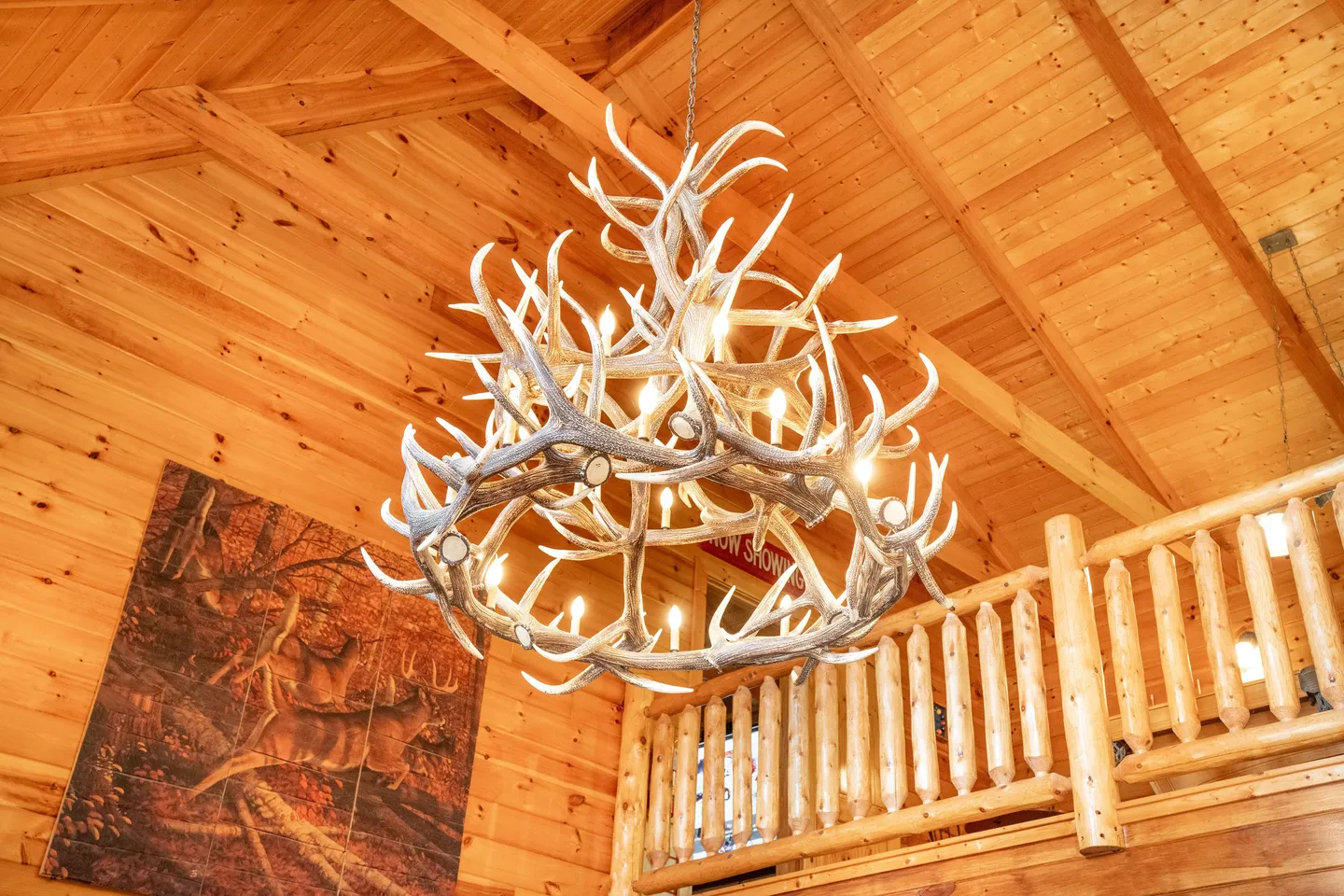 Antler chandelier hanging beneath a vaulted wood-paneled ceiling next to a log-style loft railing.
