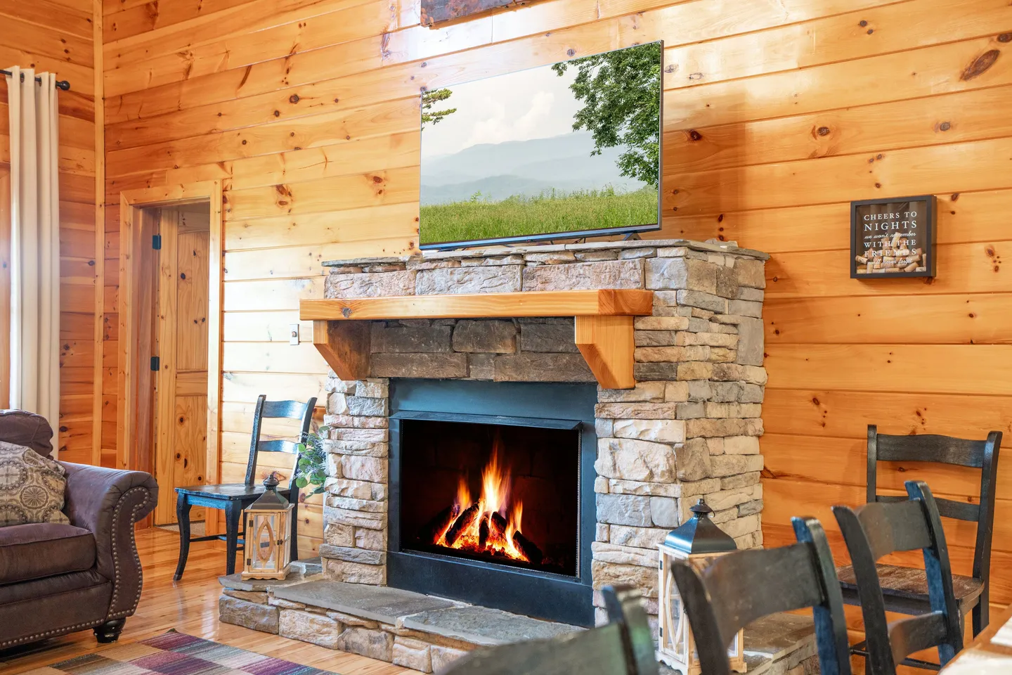 Living area with a stone fireplace, wood mantel, television, and wood-paneled walls.