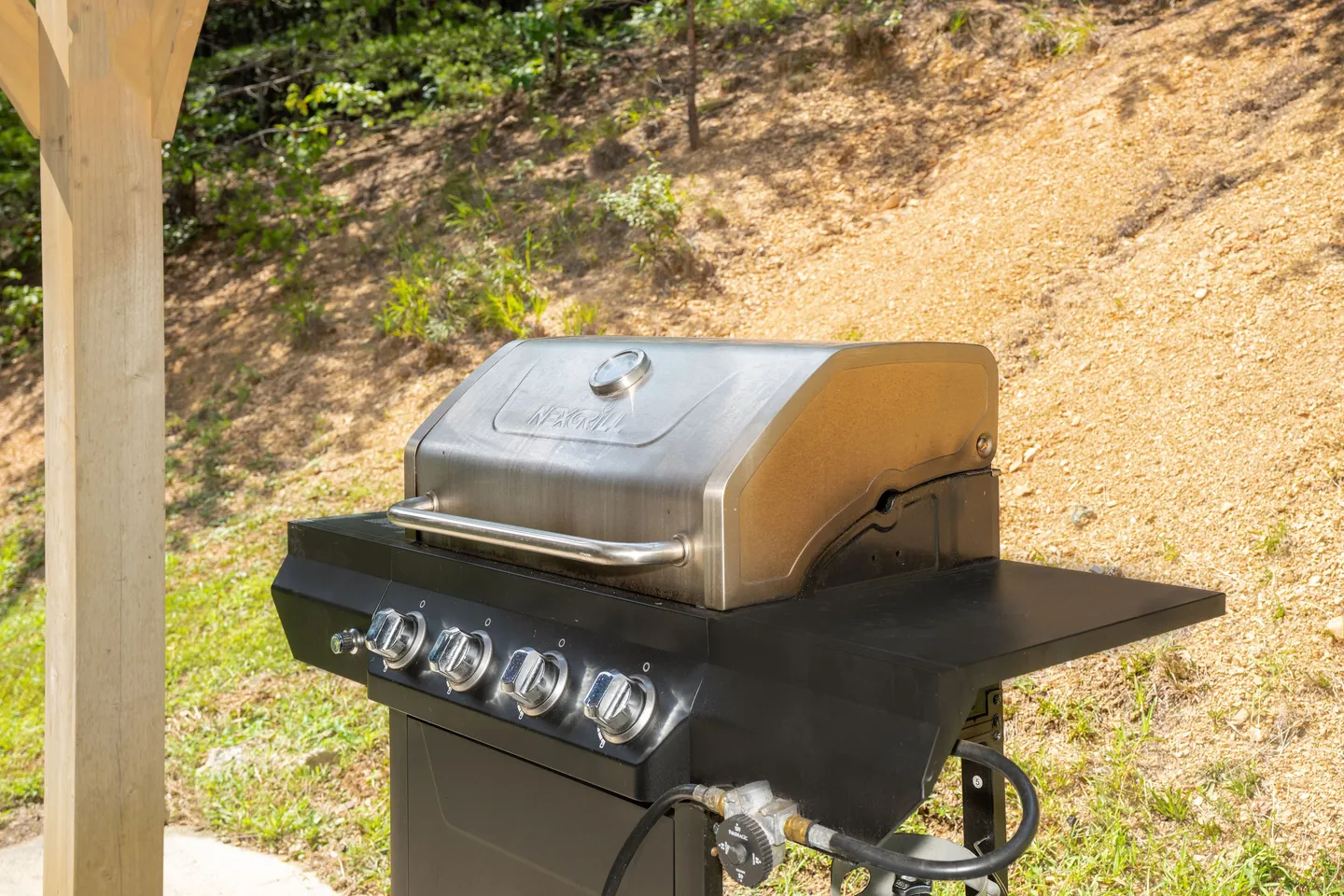 Close-up of an outdoor propane gas grill on a patio area next to a dirt hillside.