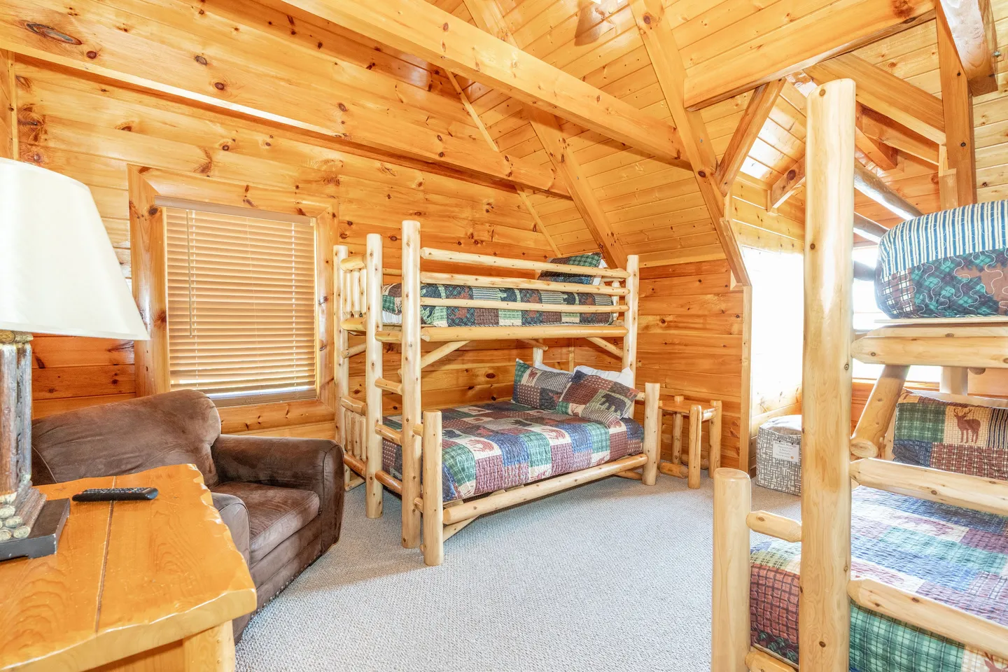 Bedroom with vaulted wood paneled ceiling, log-frame bunk beds, and an armchair.