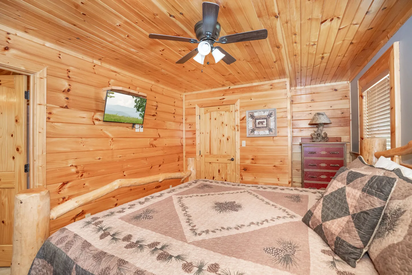 Bedroom with all-wood paneled walls and ceiling, a log bed frame, ceiling fan, and wall-mounted TV.