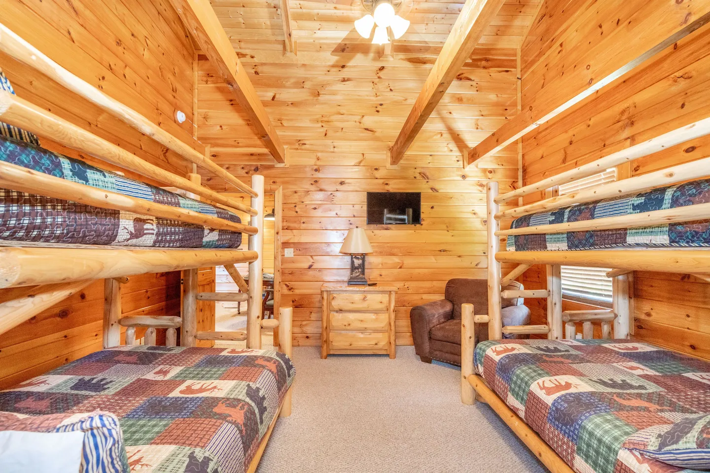 Bunk room with log-style bunk beds, wood-paneled walls, carpeted floor, and a small dresser against the back wall.