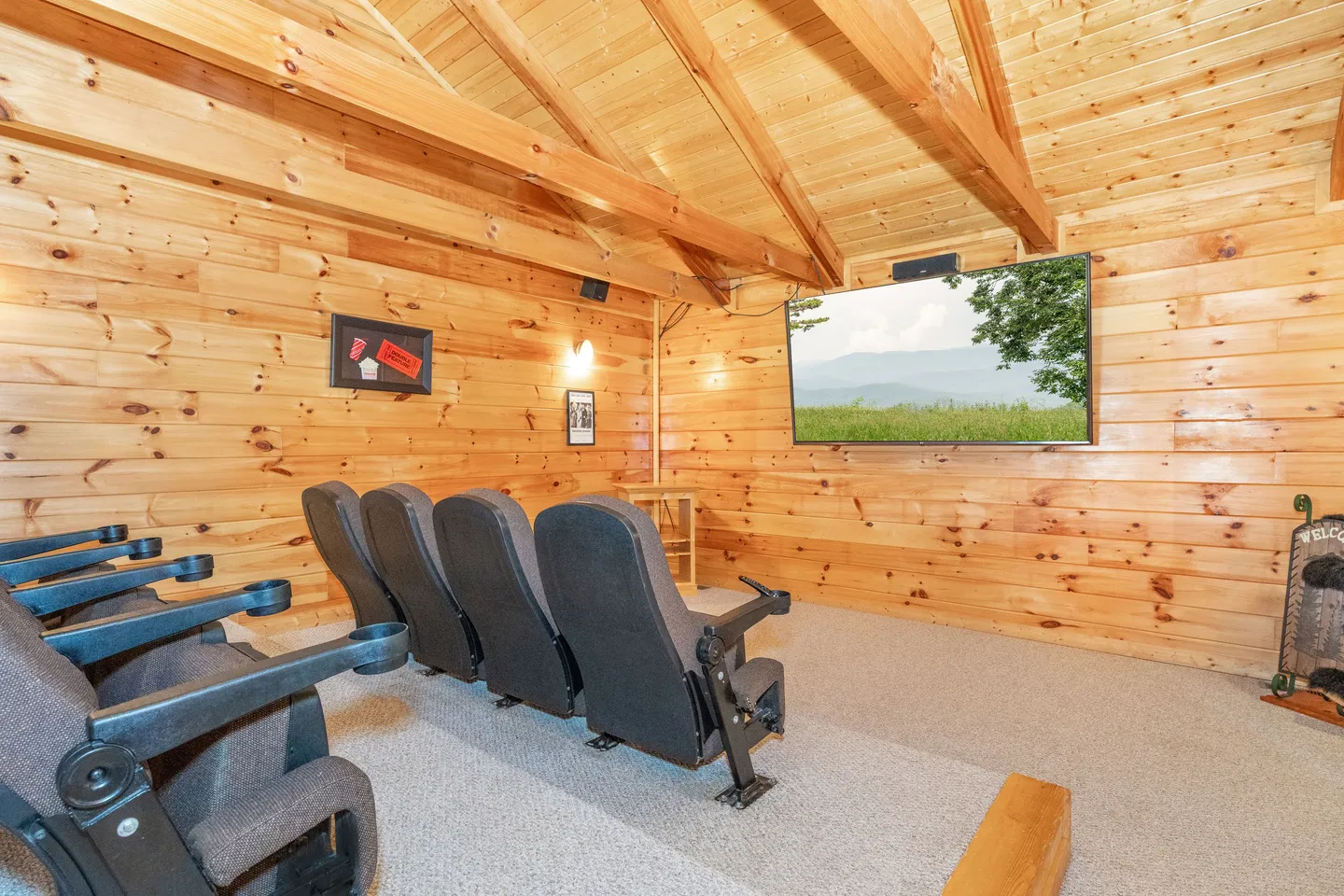 Home theater room with wood-paneled walls, vaulted beamed ceiling, rows of cinema-style seats, and a large mounted screen.