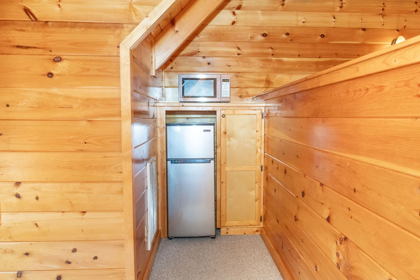 Compact alcove with wood-paneled walls featuring a mini-fridge, microwave, and small cabinet.