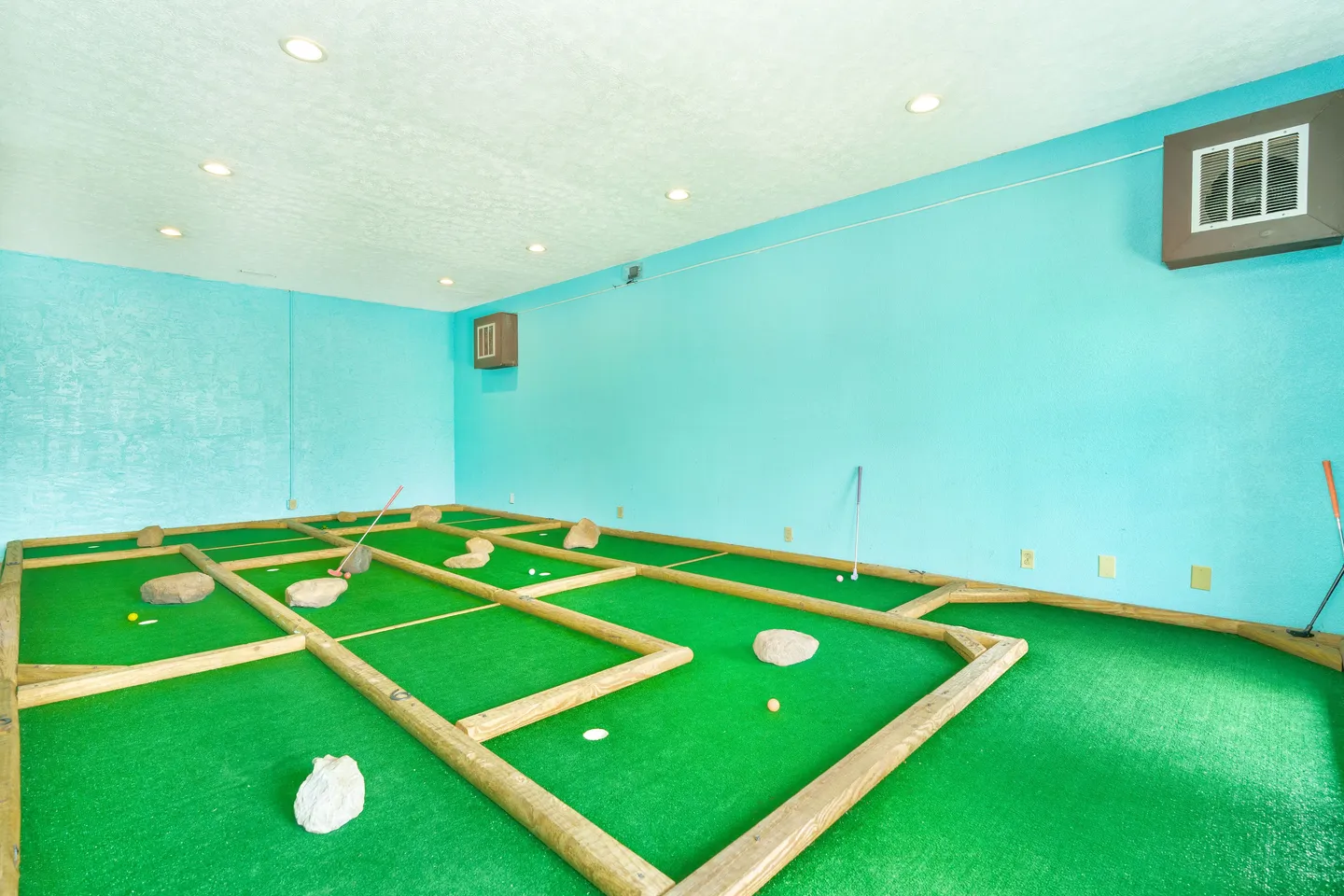 Indoor miniature golf putting green room with bright turquoise walls and artificial turf separated by wooden beams.