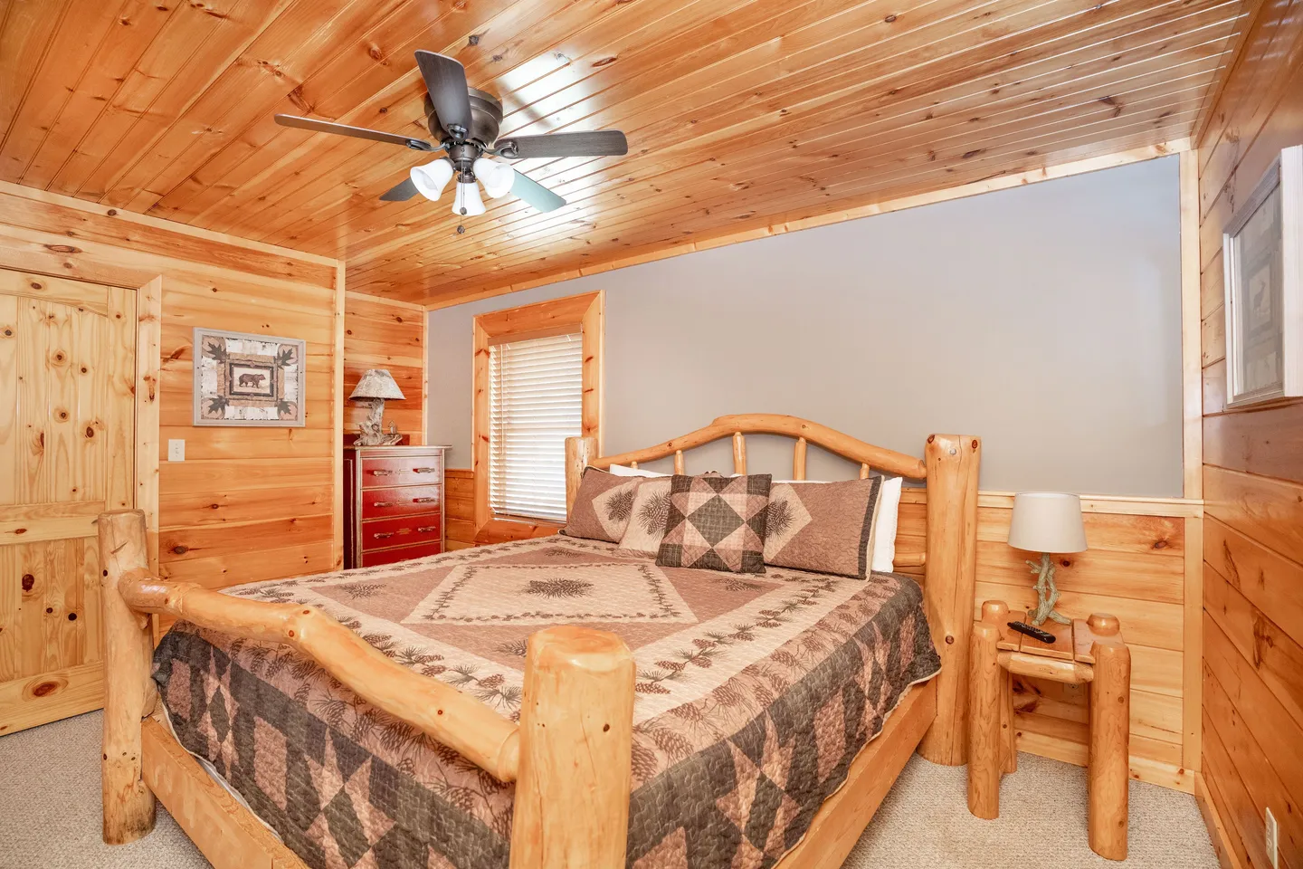 Bedroom featuring knotty pine wood paneling on the walls and ceiling, a log frame bed, and a ceiling fan.