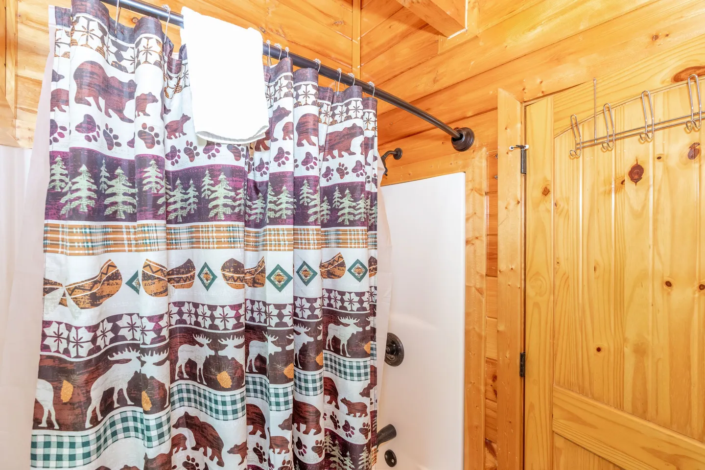 Bathroom with wood-paneled walls and a patterned shower curtain featuring bears, moose, and pine trees.
