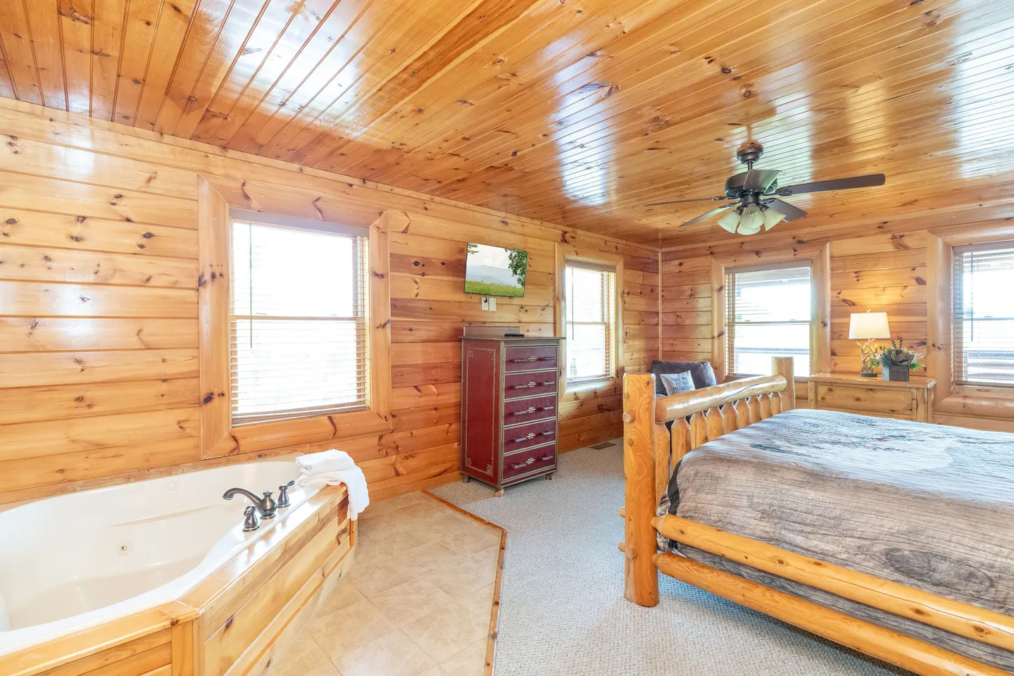 Log cabin bedroom featuring a wooden log bed, a ceiling fan, and an in-room jetted soaking tub.