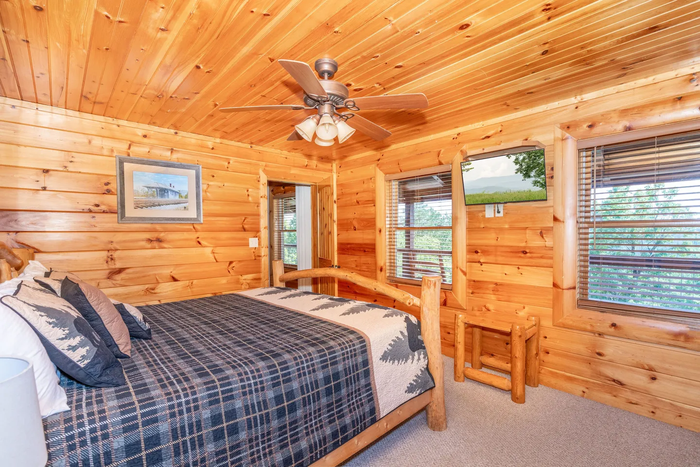 Bedroom with log walls and ceiling, carpeted floor, log-style bed, ceiling fan, and wall-mounted television.