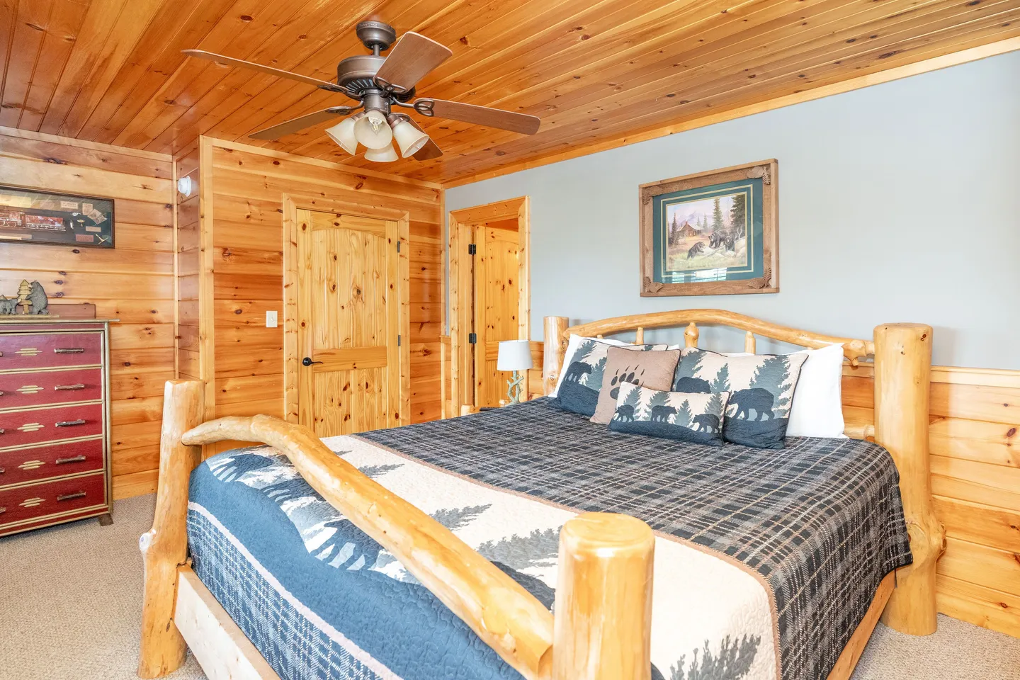Bedroom featuring a natural log bed, wood-paneled walls and ceiling, a ceiling fan, and a red dresser.