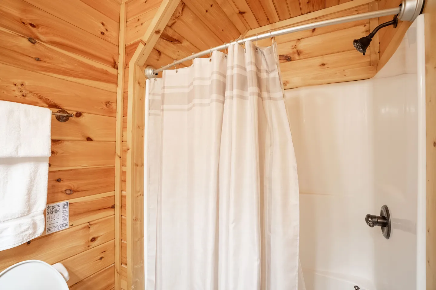 Bathroom shower with a fabric curtain framed by wood-paneled walls.