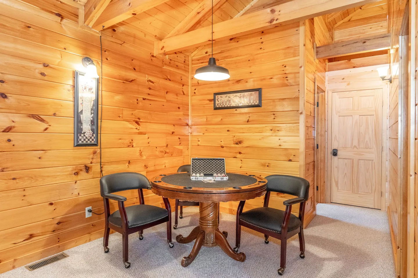 Game table with dark chairs and a poker chip set inside a wood-paneled cabin room.