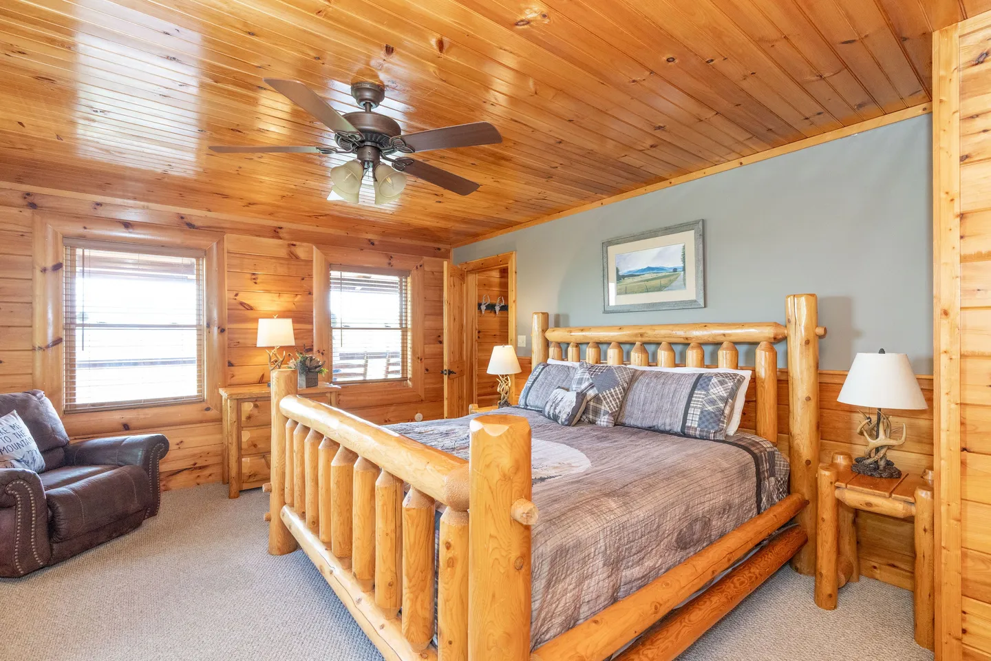 Bedroom with a log-style bed frame, wooden paneled ceiling, carpeted floor, and an armchair in the corner.