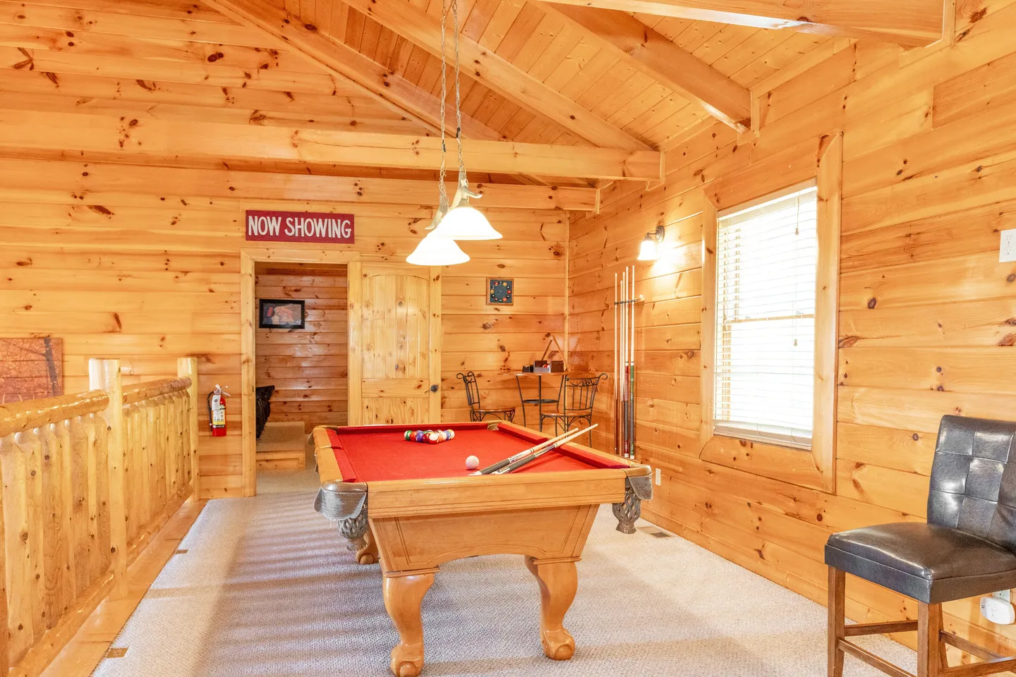 Upstairs loft game room with wood-paneled walls and ceiling, featuring a red-felt pool table.