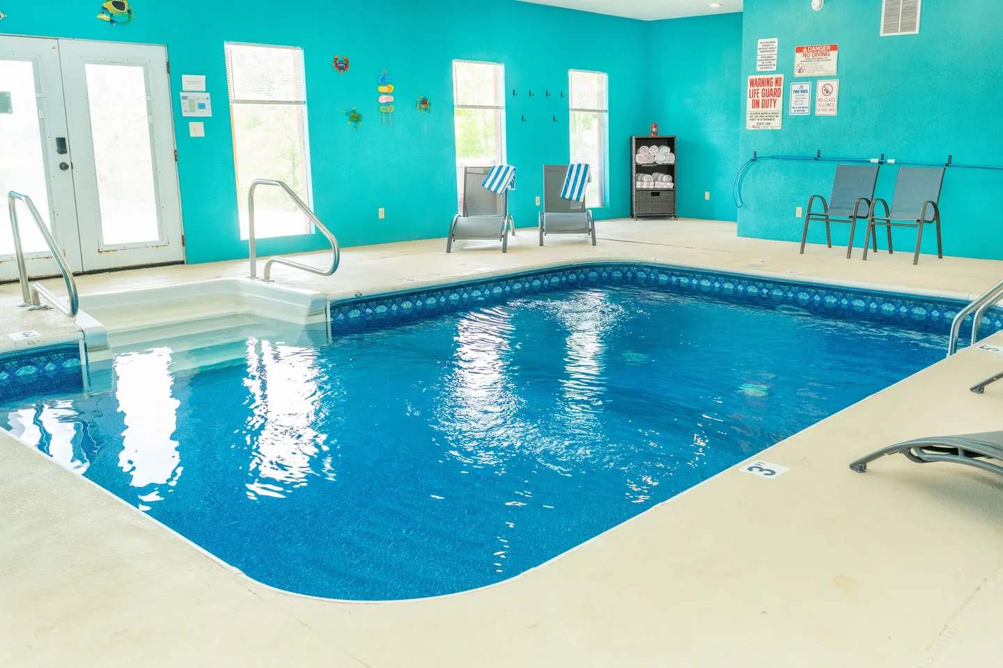 Indoor swimming pool surrounded by turquoise walls, seating, and windows with natural light.