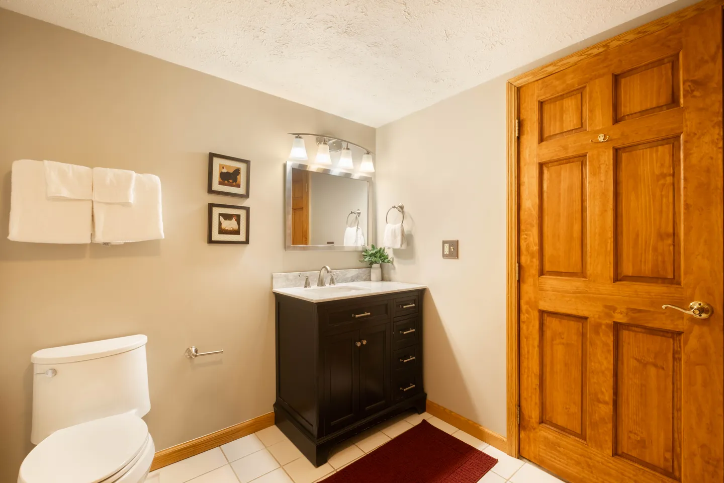 Bathroom with white toilet, dark vanity with light countertop, lighted mirror, and wooden door.