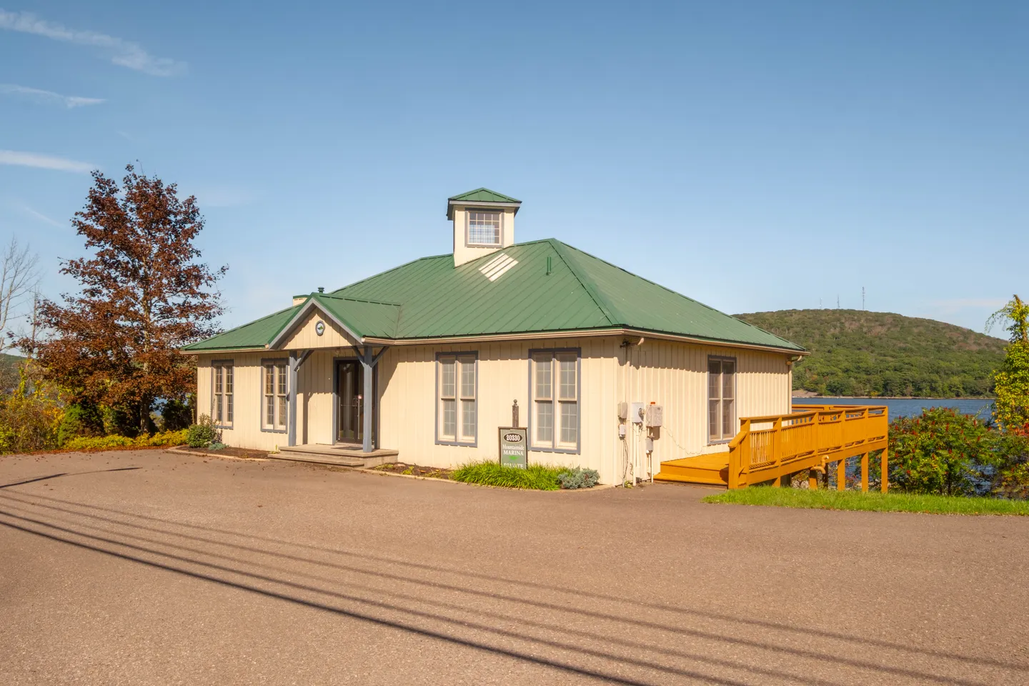 Exterior view of a single-story building with a green metal roof, light-colored siding, a cupola, and a wooden accessibility ramp on a sunny day.