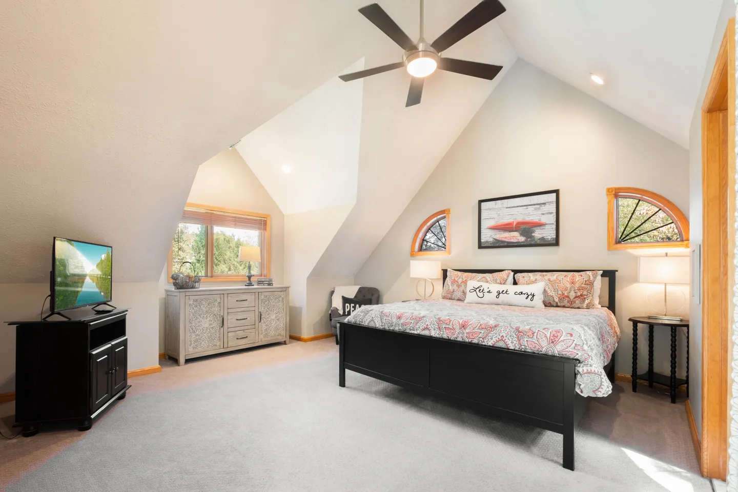 Bedroom with vaulted ceilings, a dark wood bed frame, carpeted floor, ceiling fan, and television.