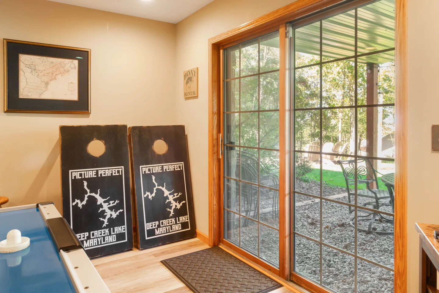 Indoor game area with an air hockey table, cornhole boards leaning against the wall, and sliding glass doors opening to an outdoor patio.