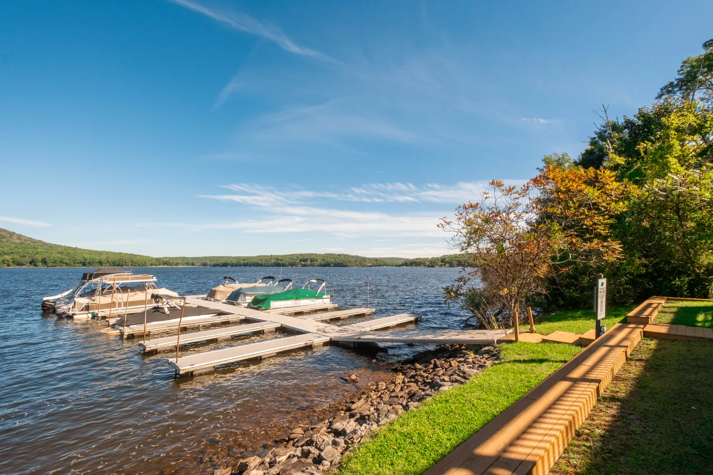 A lakeside dock extending into the water with several pontoon boats moored under a clear blue sky.