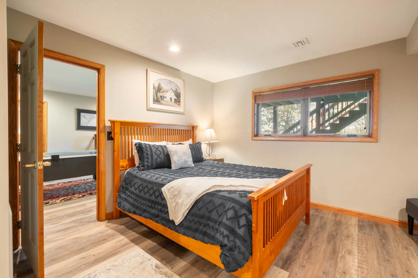 Bedroom with a wooden slat-style bed frame, dark patterned bedding, wood-look flooring, and a window.
