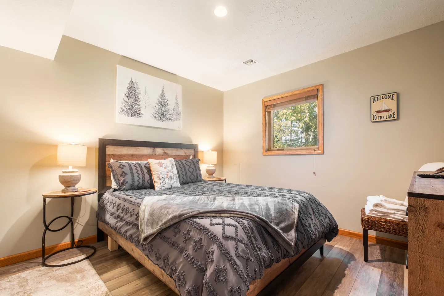 Bedroom featuring a made bed with wooden frame, rustic headboard, bedside tables with lamps, and a window.