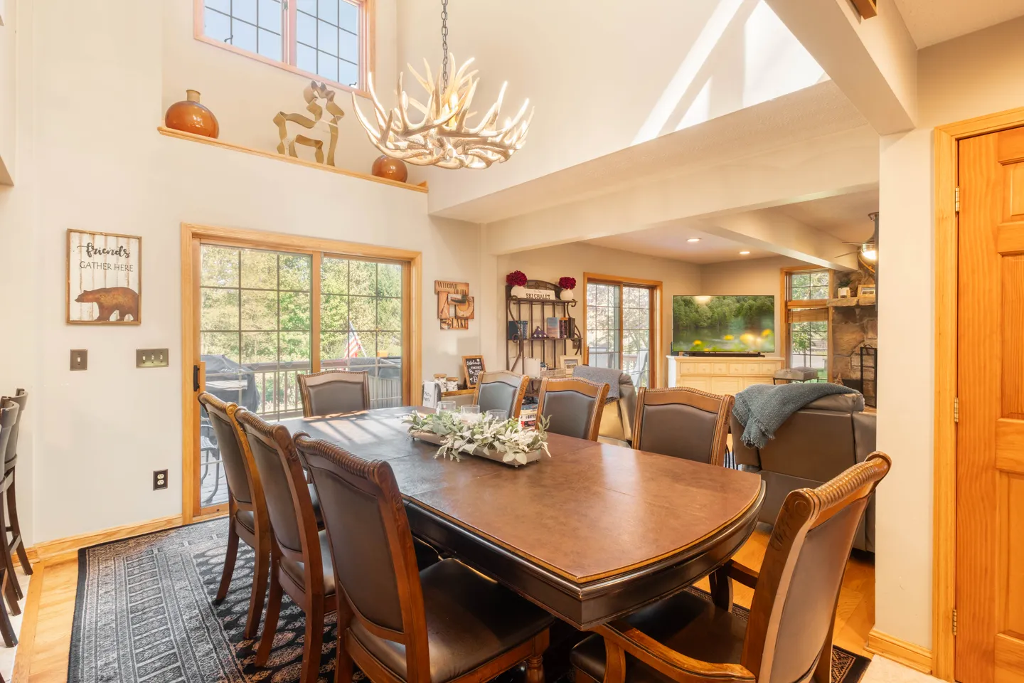 Dining area featuring a large wooden table with leather-backed chairs, an antler chandelier, and sliding glass doors to a deck.