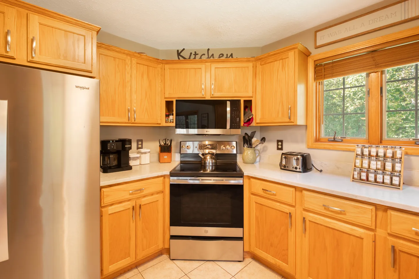 A kitchen with light wood cabinets, light countertops, and stainless steel appliances including a range, microwave, and refrigerator.