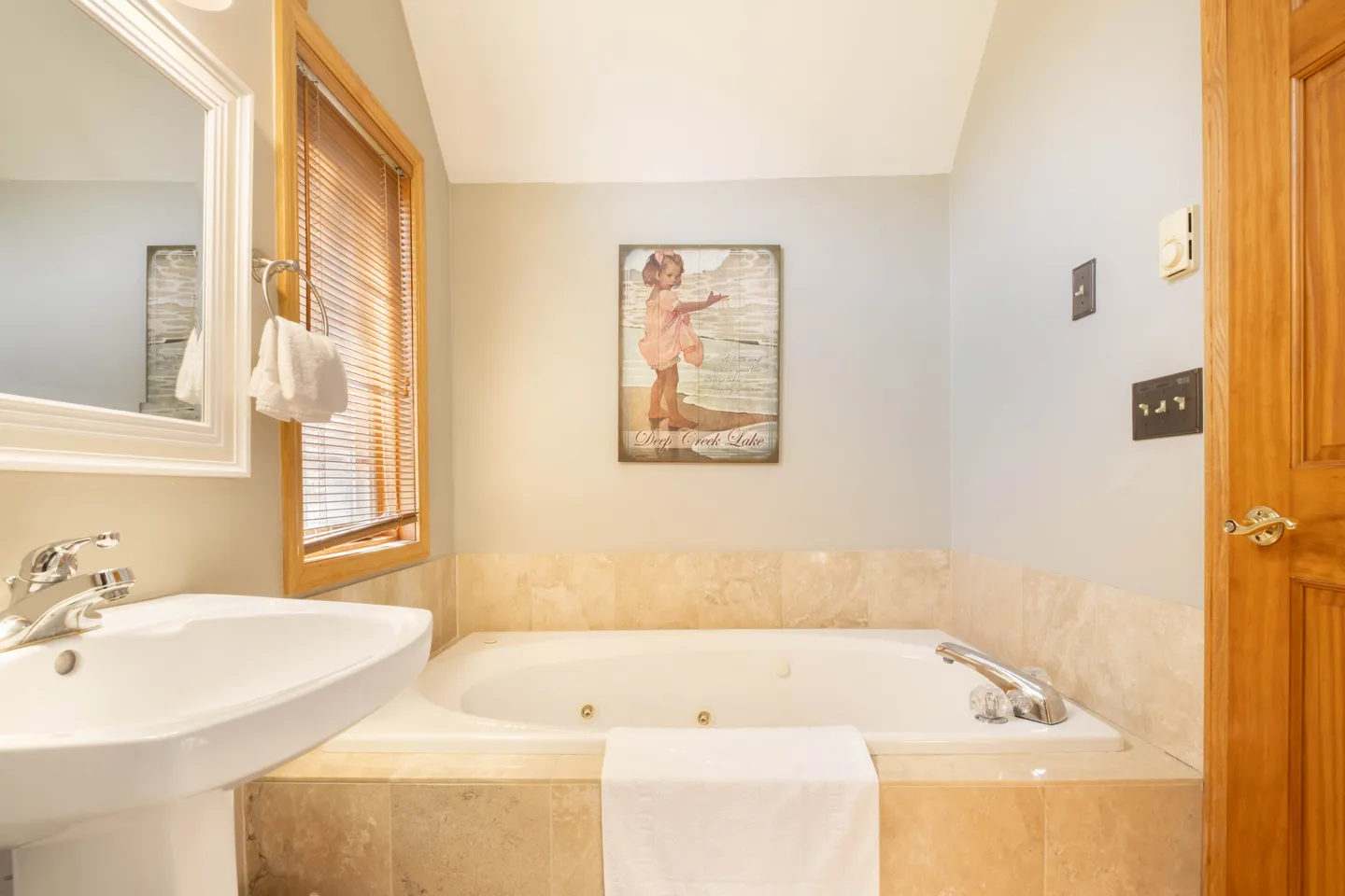 Bathroom featuring a built-in jetted tub with tile surround, a pedestal sink, and a framed mirror.