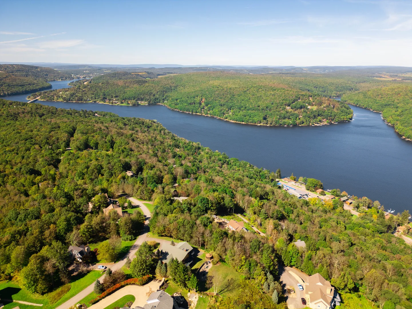 High aerial view of a wide blue lake curving through dense, rolling green hills and dotted residential neighborhoods.