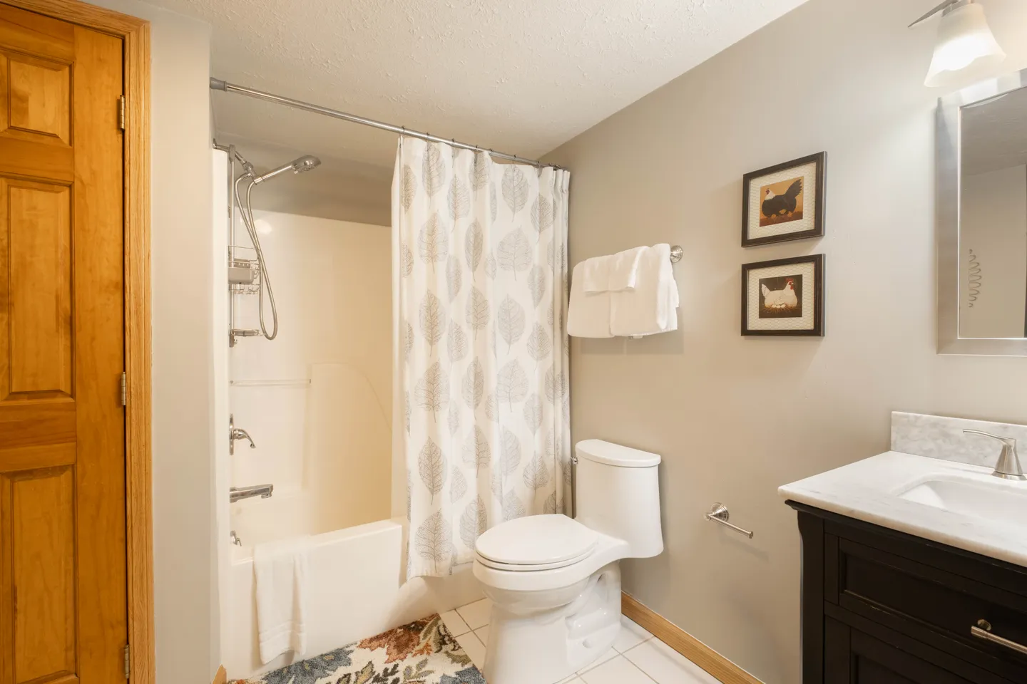 Bathroom with a bathtub and shower combination, white toilet, and dark vanity with marble top.