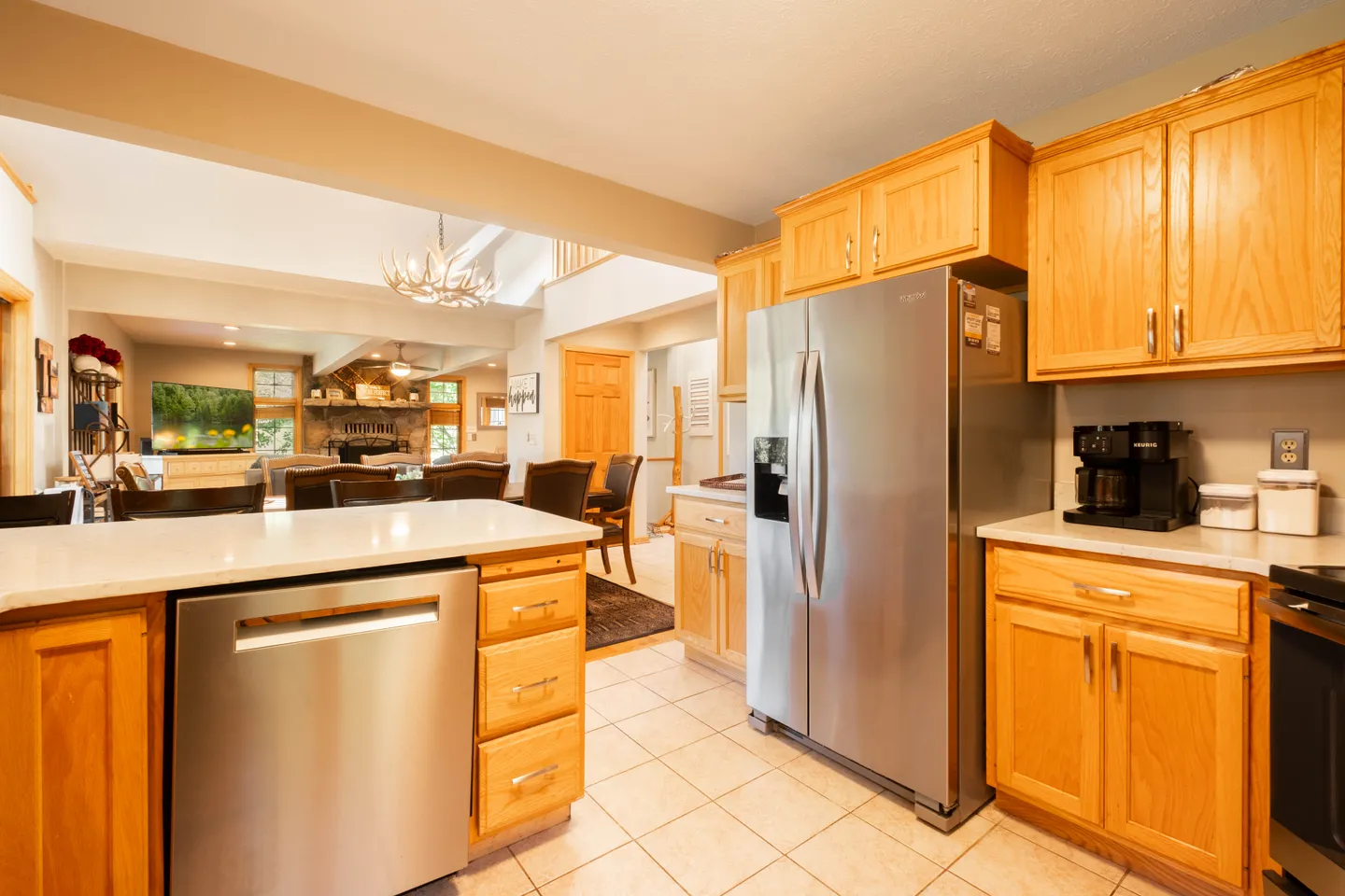 Kitchen with oak cabinets, stainless steel appliances, and tiled floors looking into the dining and living area.
