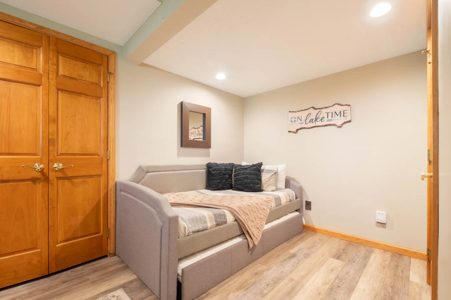 A small alcove bedroom featuring an upholstered daybed with a trundle, wood-look flooring, and a wooden double door closet.